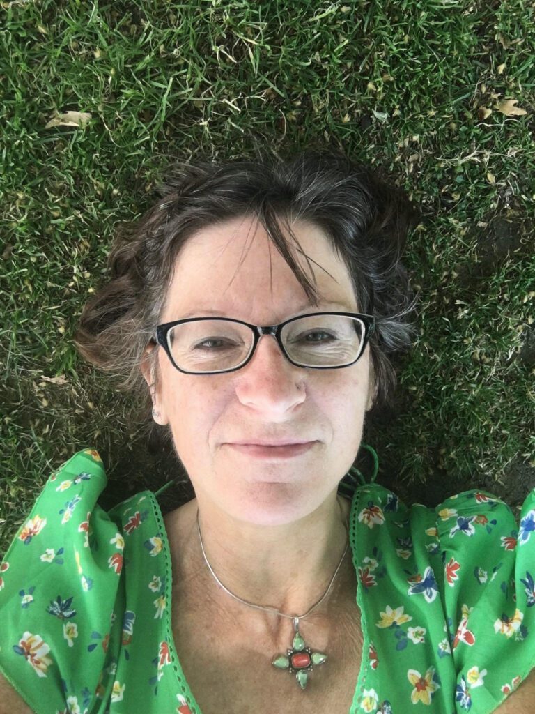 A portrait of Abi. She is wearing a green dress and lying on the grass smiling at the camera.